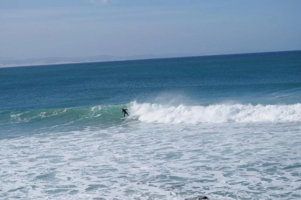 Surfer riding waves on pristine beach with clear blue ocean horizon