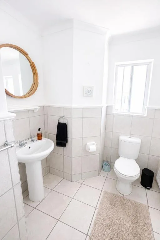 Clean white bathroom with pedestal sink, toilet, and round mirror