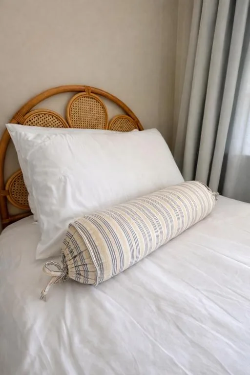 Bed with white pillows and striped bolster, wooden rattan headboard