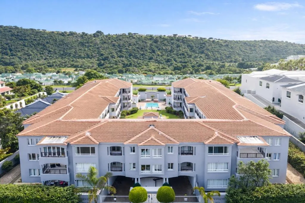 White apartment building with terracotta roof overlooking lush valley and lagoon