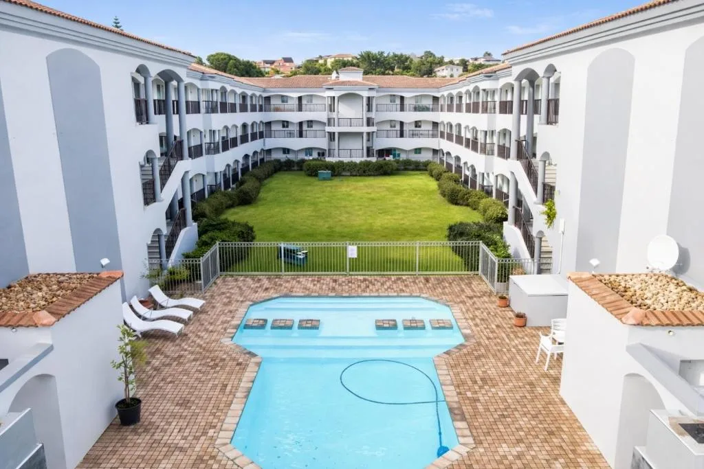 White Mediterranean-style apartment complex with central courtyard, pool, and manicured lawn