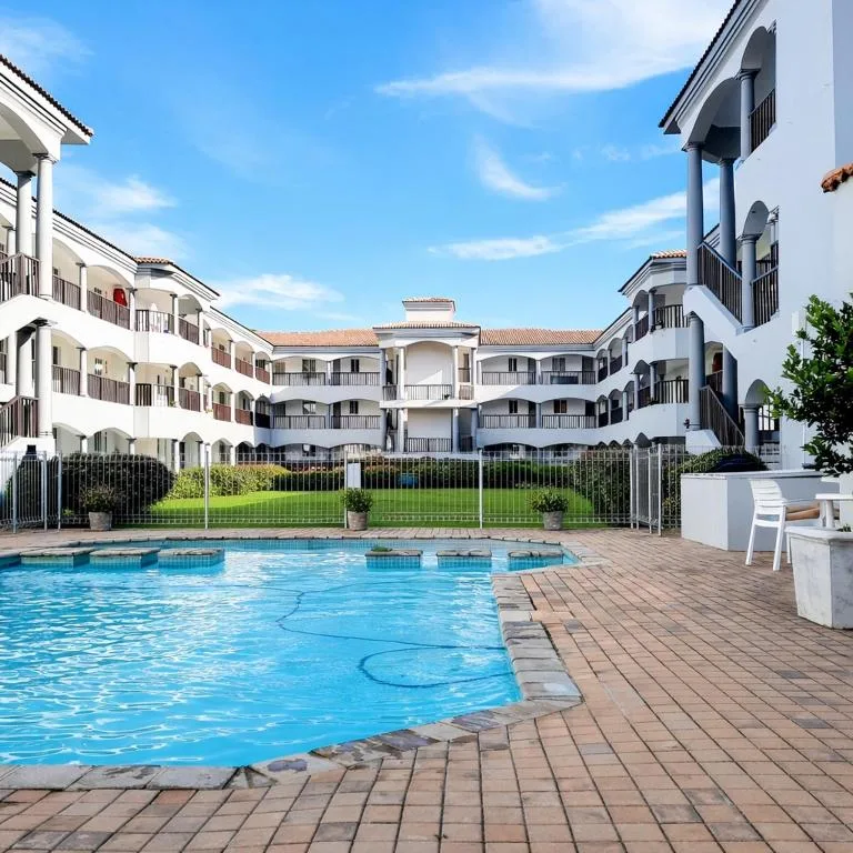 Sparkling swimming pool surrounded by manicured lawn and modern white apartment building