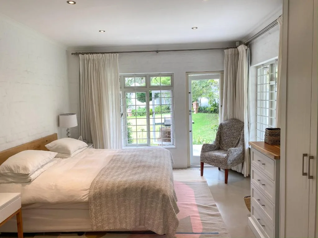 Bright bedroom with queen bed, garden views through French doors, comfortable seating area