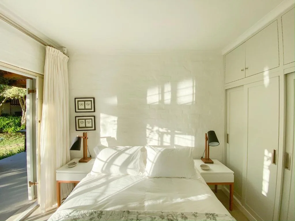 Bright bedroom with queen bed, white bedding, wooden nightstands, and garden view