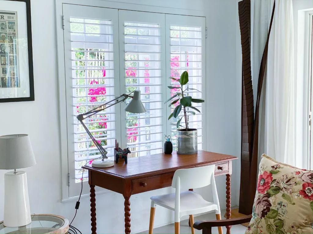 Wooden desk with task lamp and plant near shuttered windows