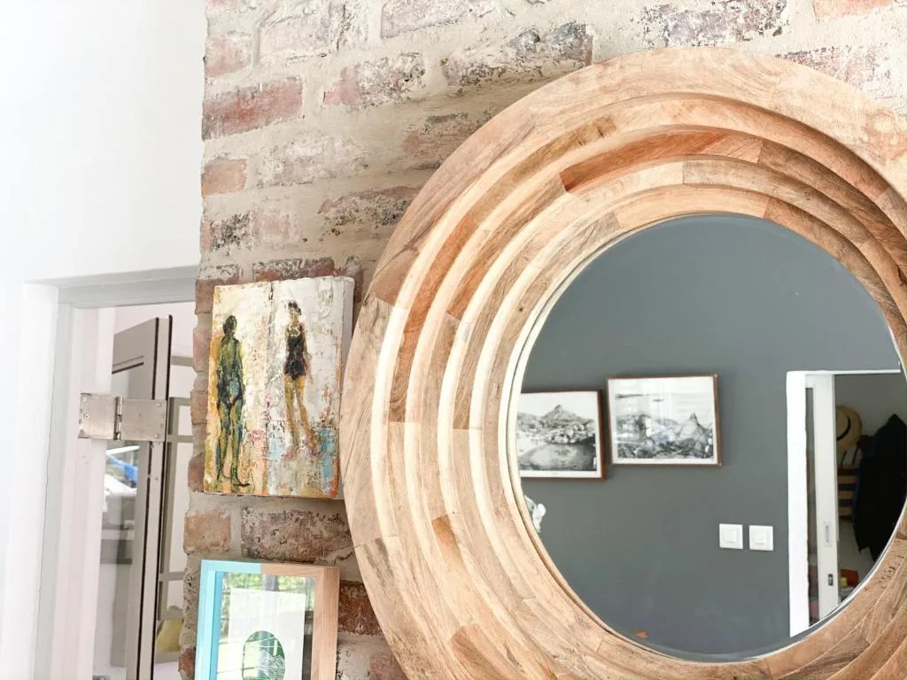Large wooden-framed circular mirror leaning against rustic brick wall