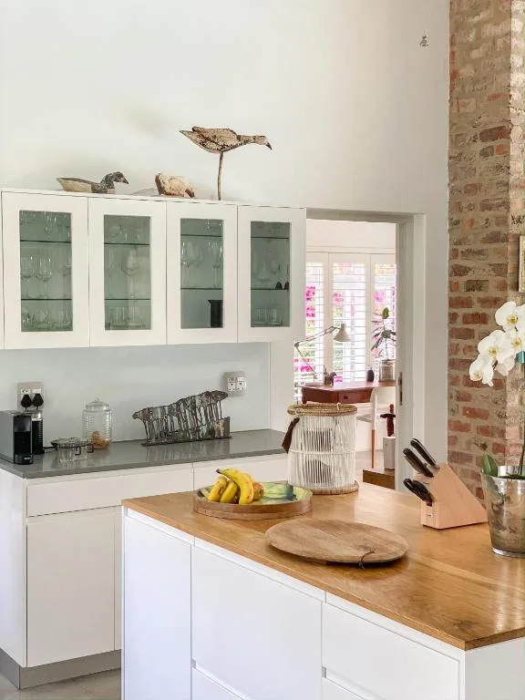 Modern kitchen with white cabinetry, wood countertop island, and exposed brick wall