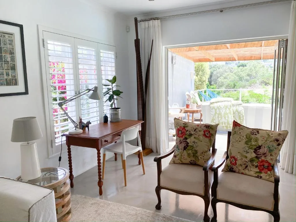 Bright lounge with floral chairs, desk, and garden views through glass doors