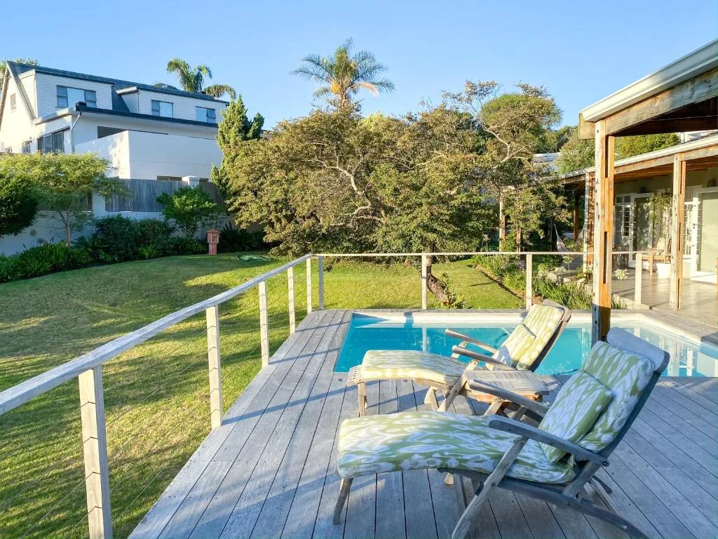 Wooden deck with lounge chairs overlooking swimming pool and garden