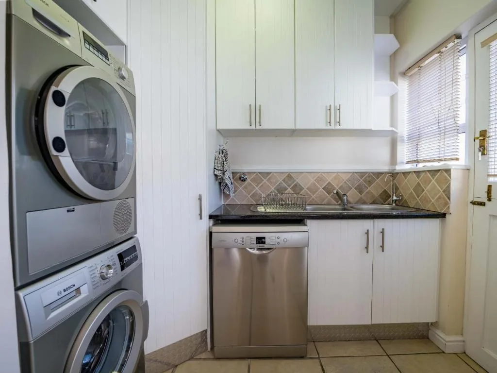 Modern laundry room with stacked washer and dryer, dishwasher, white cabinetry