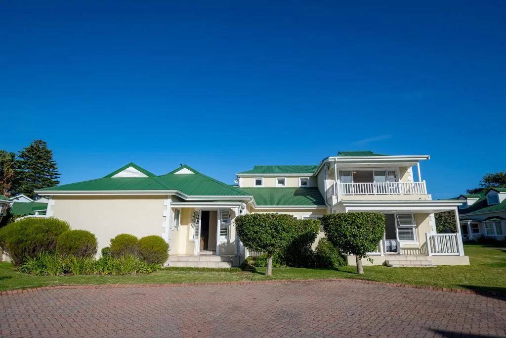Cream-colored house with green roof and manicured lawn frontage