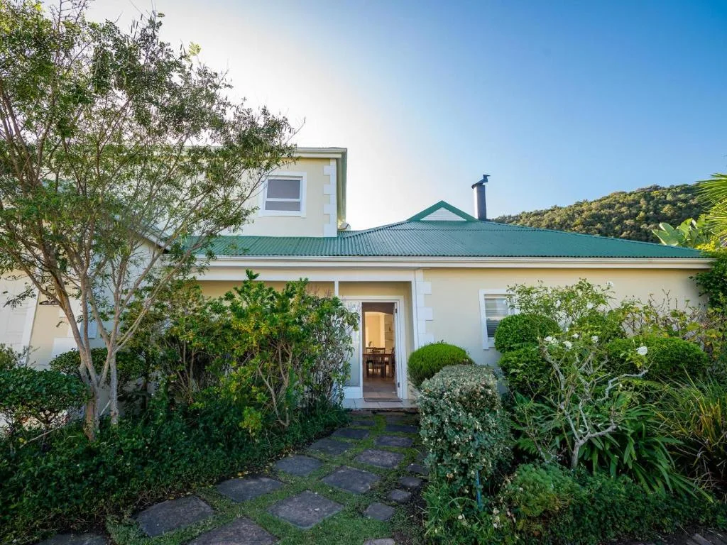 White cottage with turquoise roof and manicured garden entrance