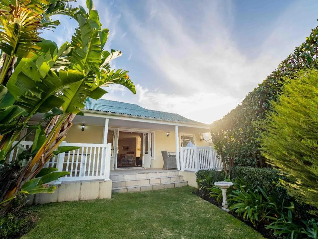Charming cottage with white veranda, green roof, surrounded by lush tropical gardens