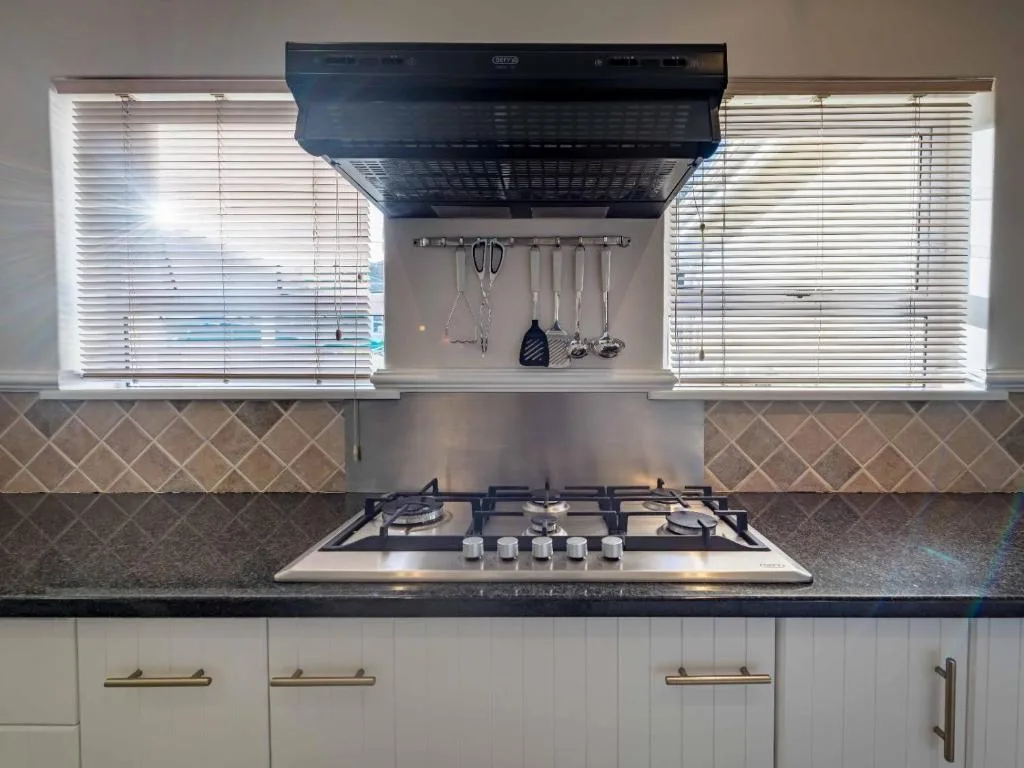 Modern kitchen with gas cooktop, black hood, dark countertop, and white cabinetry