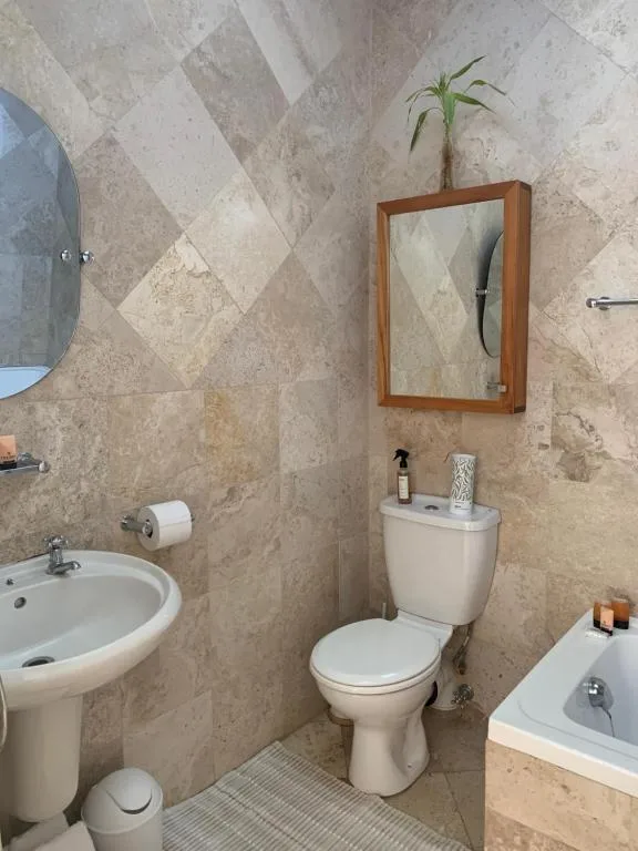 Modern bathroom with beige tile walls, white toilet, pedestal sink, and wooden-framed mirror