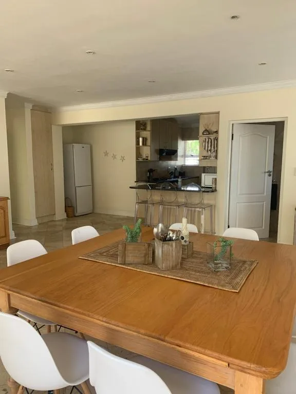 Wooden dining table with white chairs, kitchen visible beyond