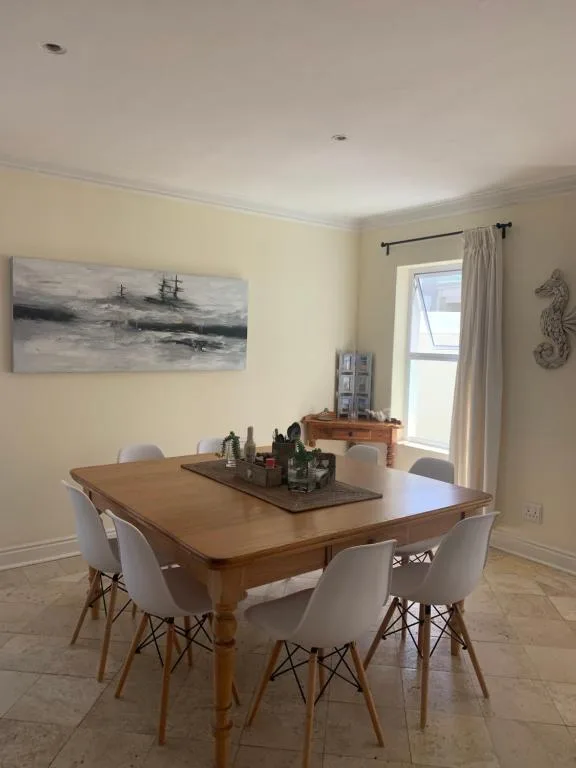 Wooden dining table with white chairs and coastal artwork above