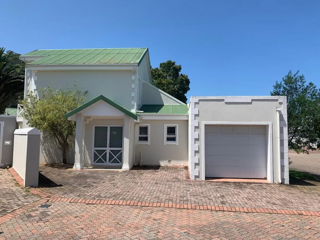 Modern white cottage with green roof and attached garage on brick driveway