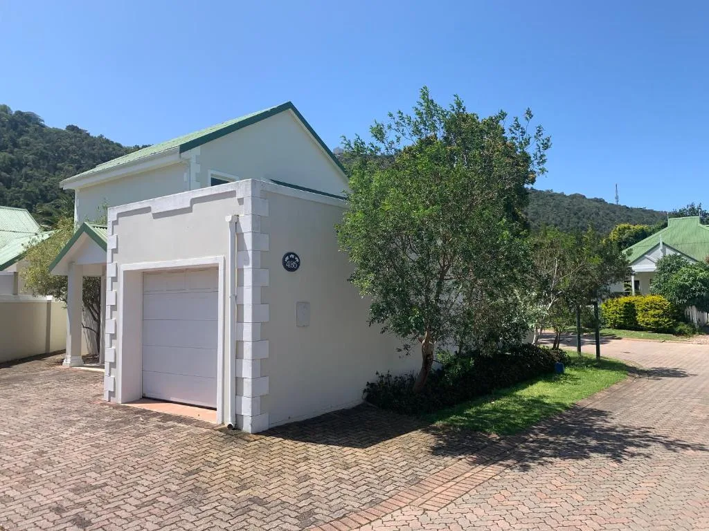 White modern cottage with garage and green-roofed buildings surrounded by trees