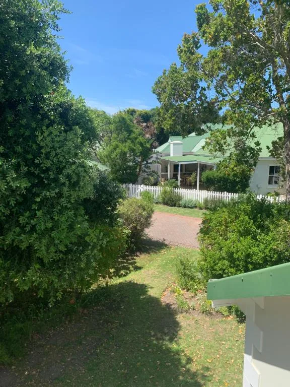 White cottage with green roof nestled among lush garden trees