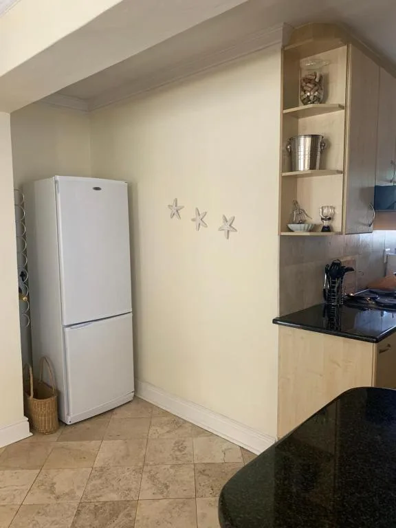 Kitchen corner with white refrigerator, black countertop, and open shelving