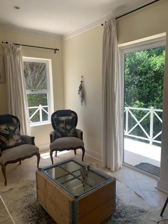 Bright lounge with upholstered chairs and glass coffee table, opening to deck