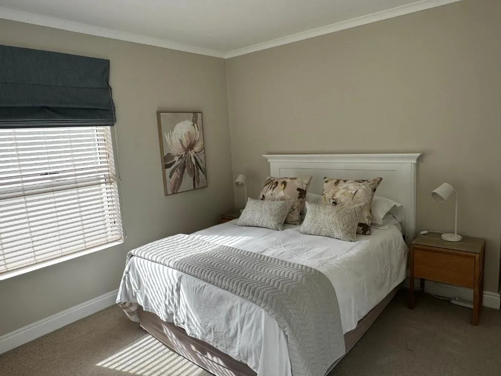 Bright bedroom with white headboard bed, neutral bedding, and wooden nightstand
