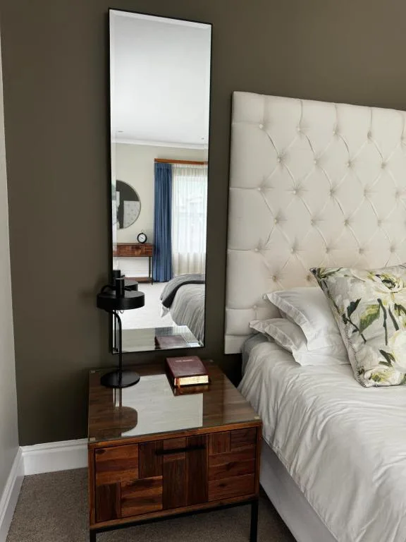 Bedroom with upholstered headboard, wooden dresser, and large mirror