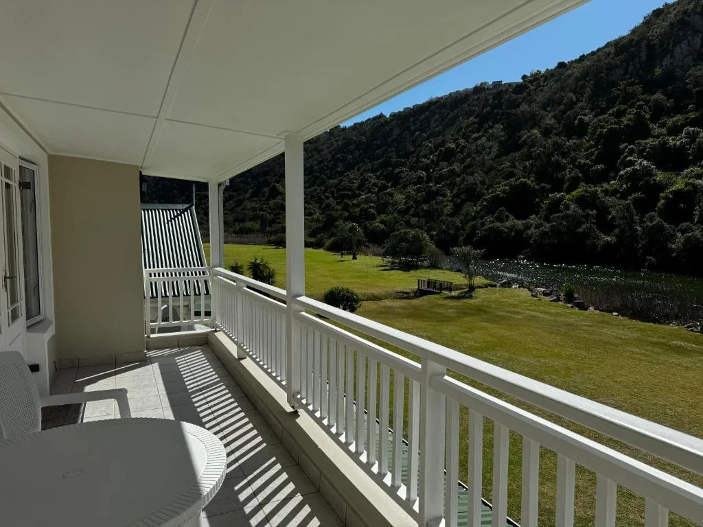 Covered deck with white railings overlooking expansive green lawn and forest-clad hills