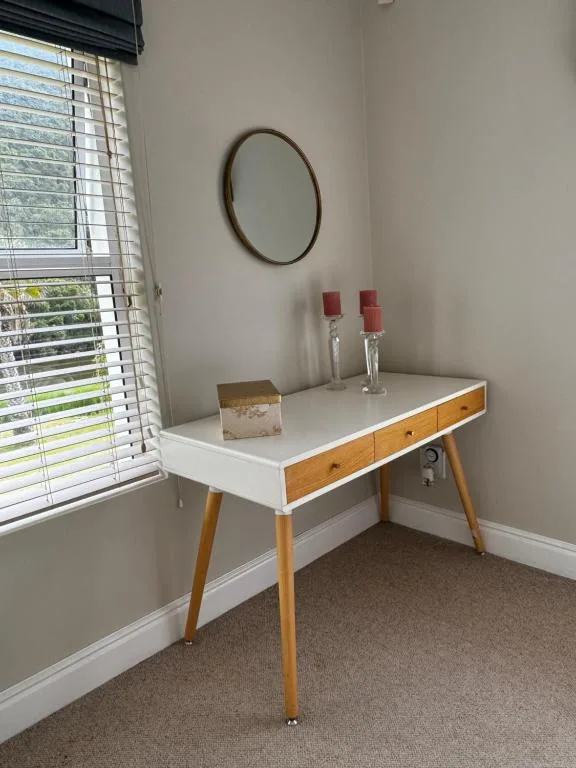 Mid-century wooden desk with white top, round mirror, and decorative candles