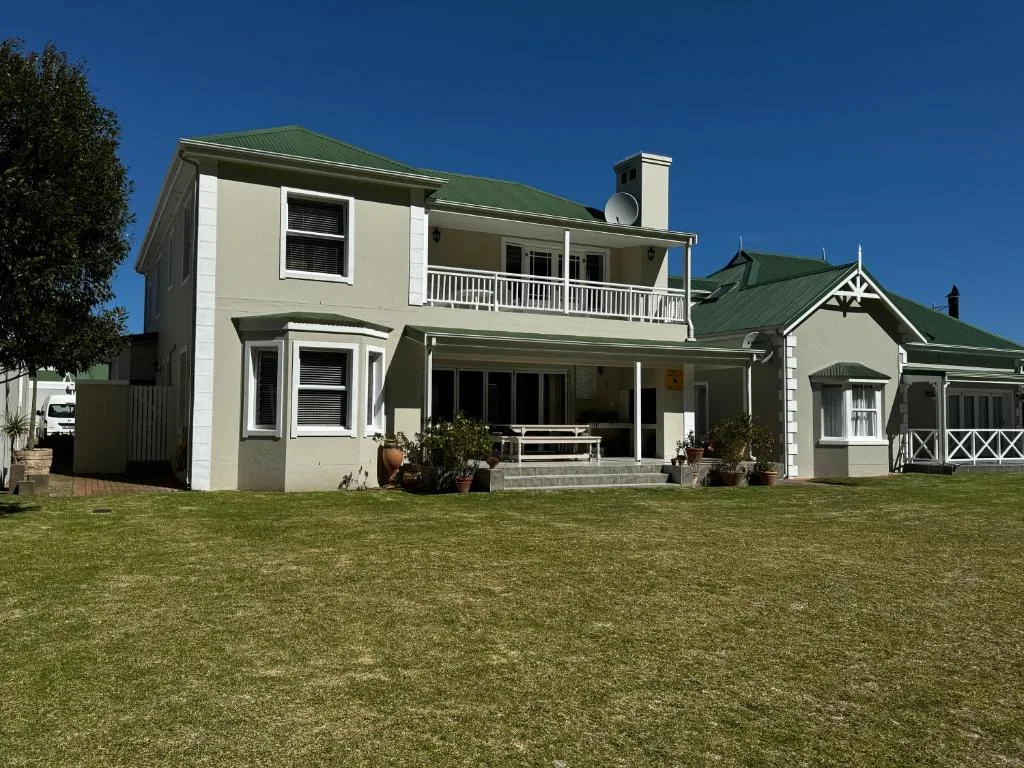 Cream and green cottage with manicured lawn and clear blue sky