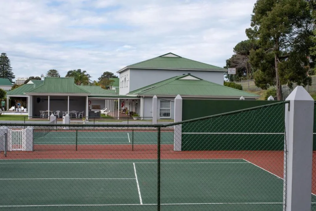 White house with green roof and covered deck overlooking tennis courts