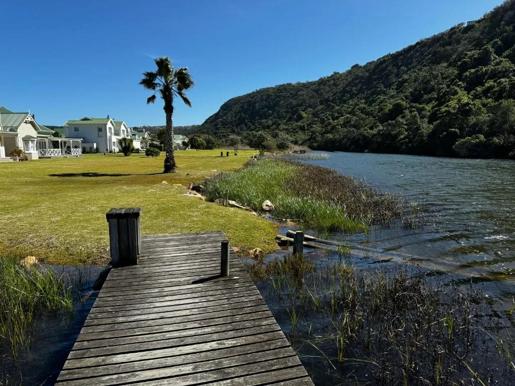 Lagoon view with forested mountains, wooden jetty, and white cottage beyond
