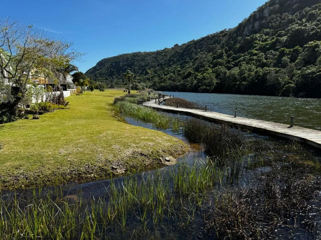 Scenic river valley with forested mountains, lush gardens and wooden jetty