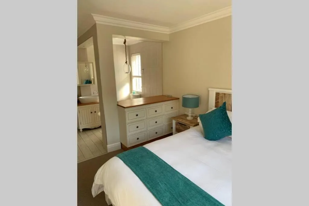 Spacious bedroom with white bed, teal accents, and ensuite bathroom visible