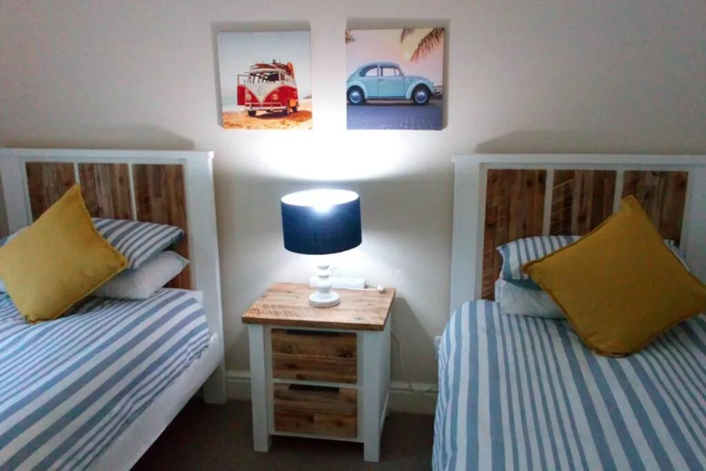Twin bedroom with striped bedding, yellow pillows, wooden nightstand and lamp