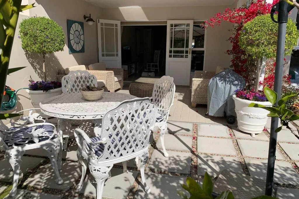 Shaded patio with white metal chairs, dining table, and vibrant potted flowers