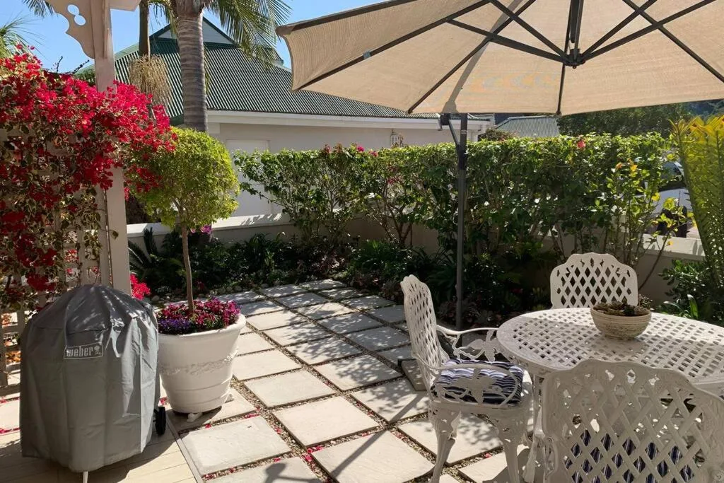 Spacious patio with white furniture, large umbrella, and vibrant red bougainvillea flowers