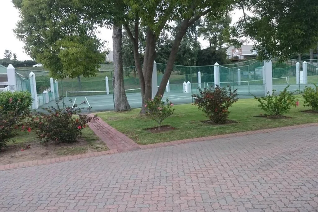 Brick paved driveway with mature trees and manicured gardens, tennis court visible