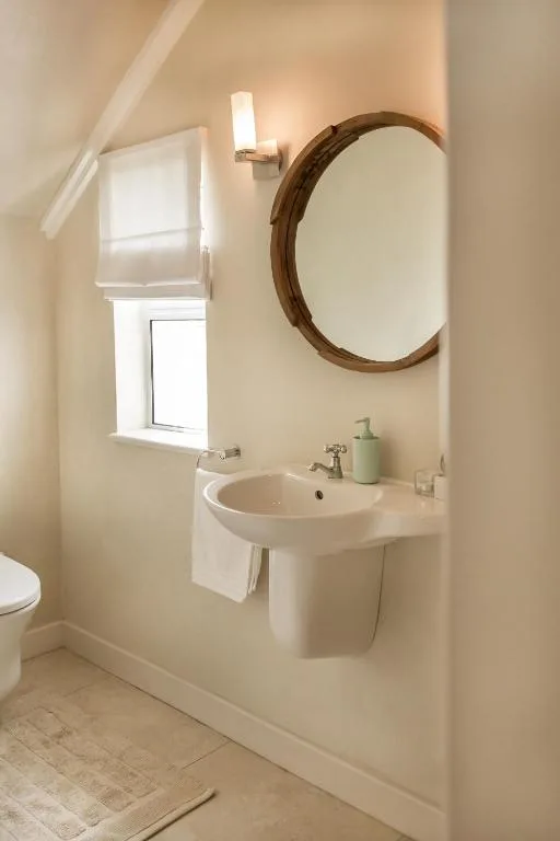Bright bathroom with round wooden mirror and pedestal sink