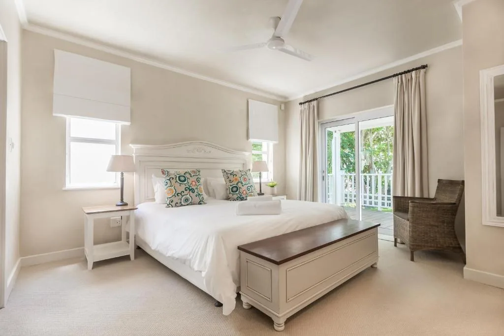 Bright bedroom with white bed frame and patterned cushions, opening to deck