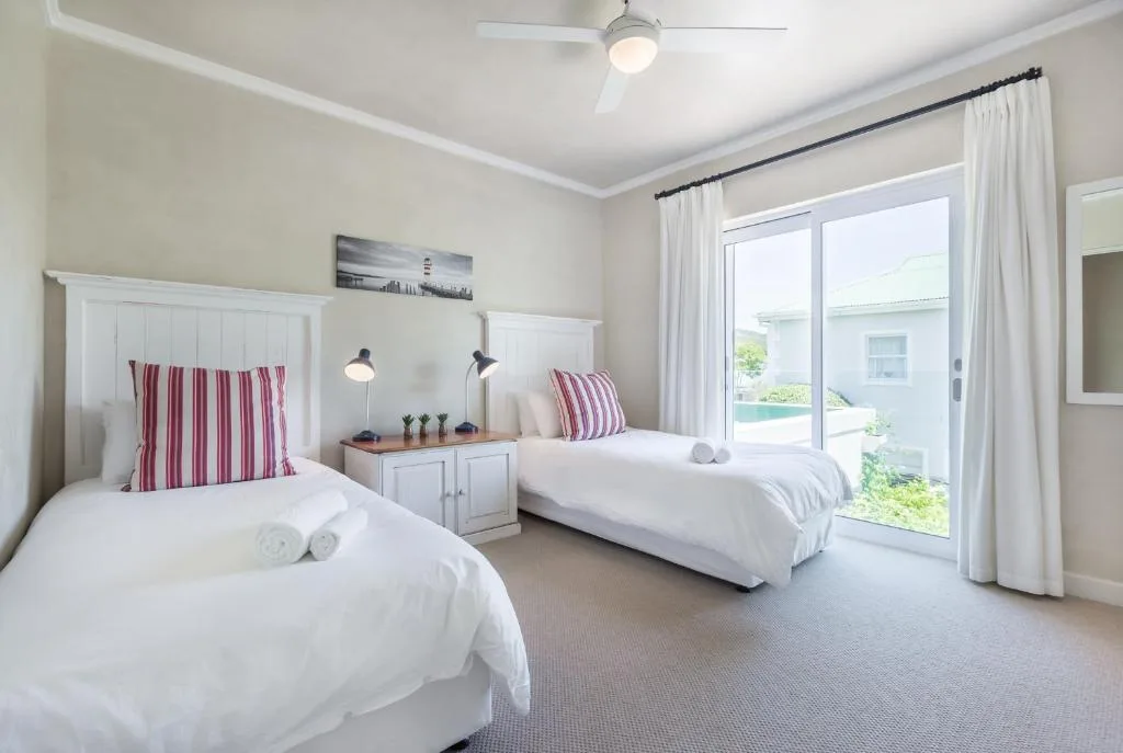 Bright twin bedroom with white beds, red striped pillows, and garden views