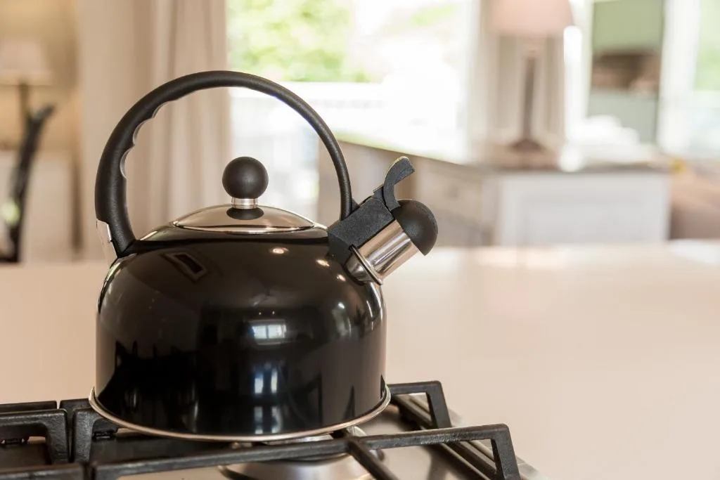 Black whistling kettle on gas stovetop in modern kitchen