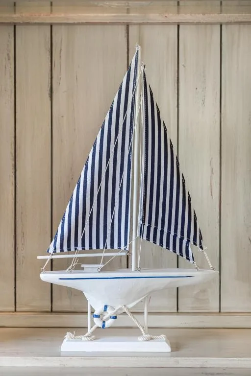 Decorative white sailboat model with navy striped sail on wooden shelf