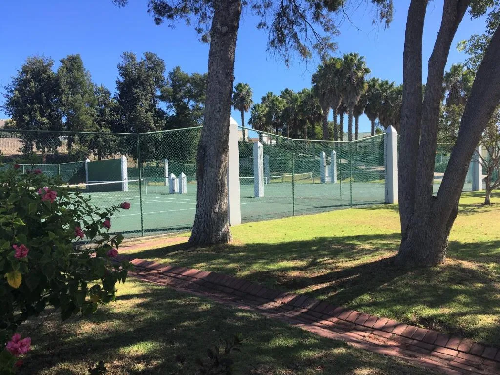 Tennis court surrounded by mature trees and flowering gardens on property