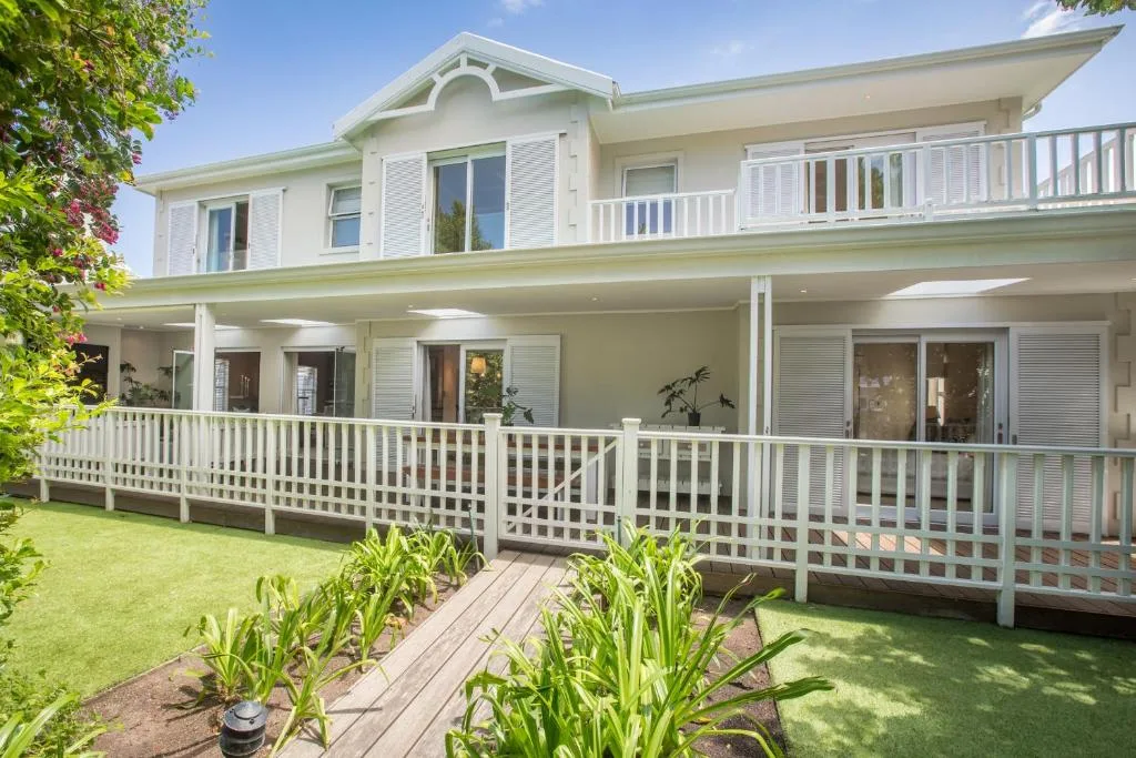 Two-story white beach house with wraparound deck and manicured lawn