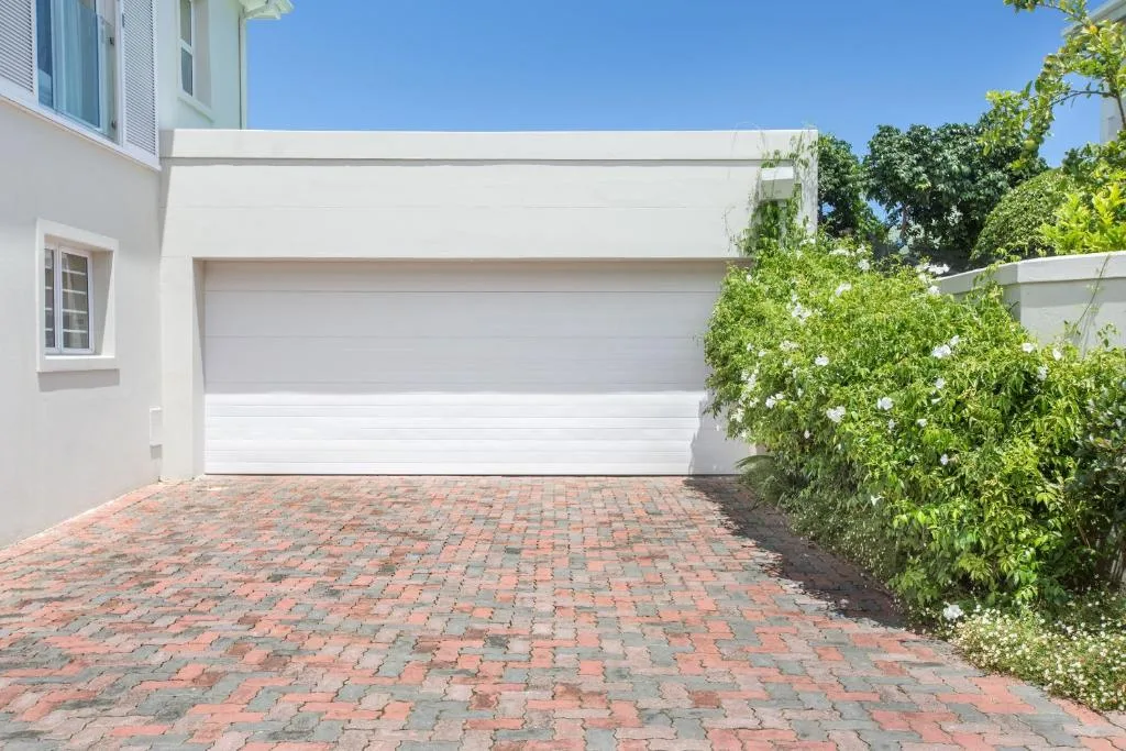 White garage with brick driveway and climbing ivy vines