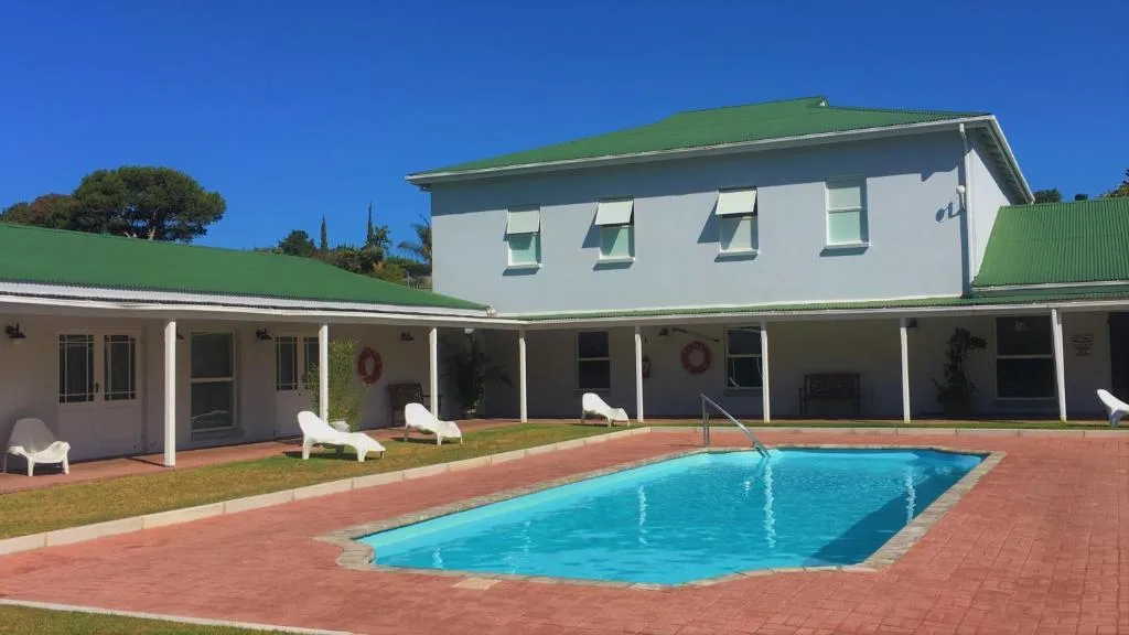 Swimming pool with brick patio, white loungers, and modern house behind