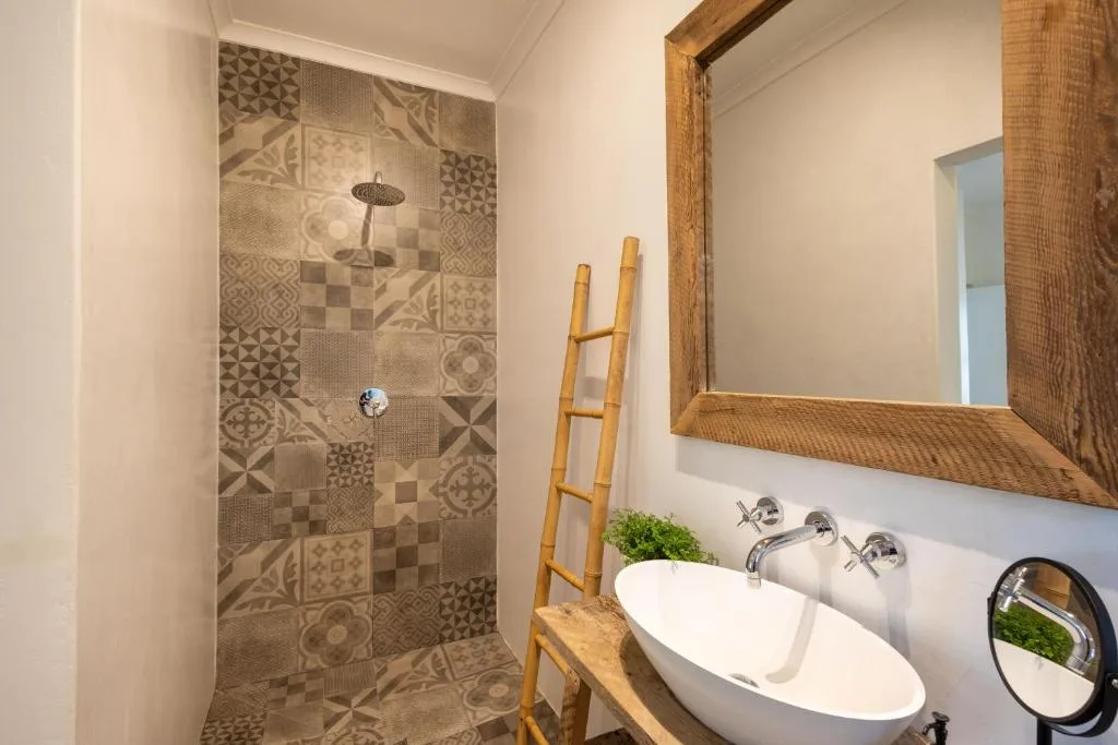 Modern bathroom with patterned tile shower, white oval sink, wooden mirror frame