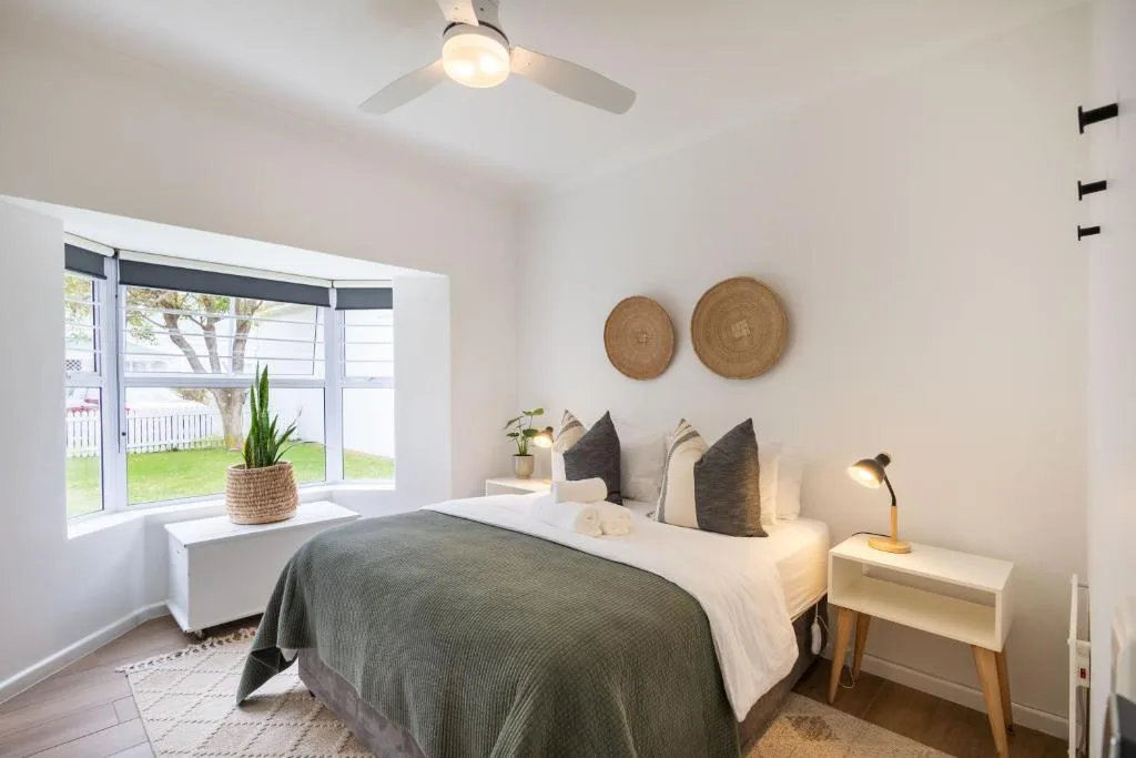 Bright bedroom with made bed, woven wall art, and garden view through glass doors